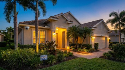 Florida home exterior at dusk showing visible security camera and security company yard sign near a well-lit front entrance
